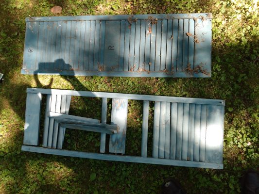 Two old, deteriorating wood shutters lie on the grass.