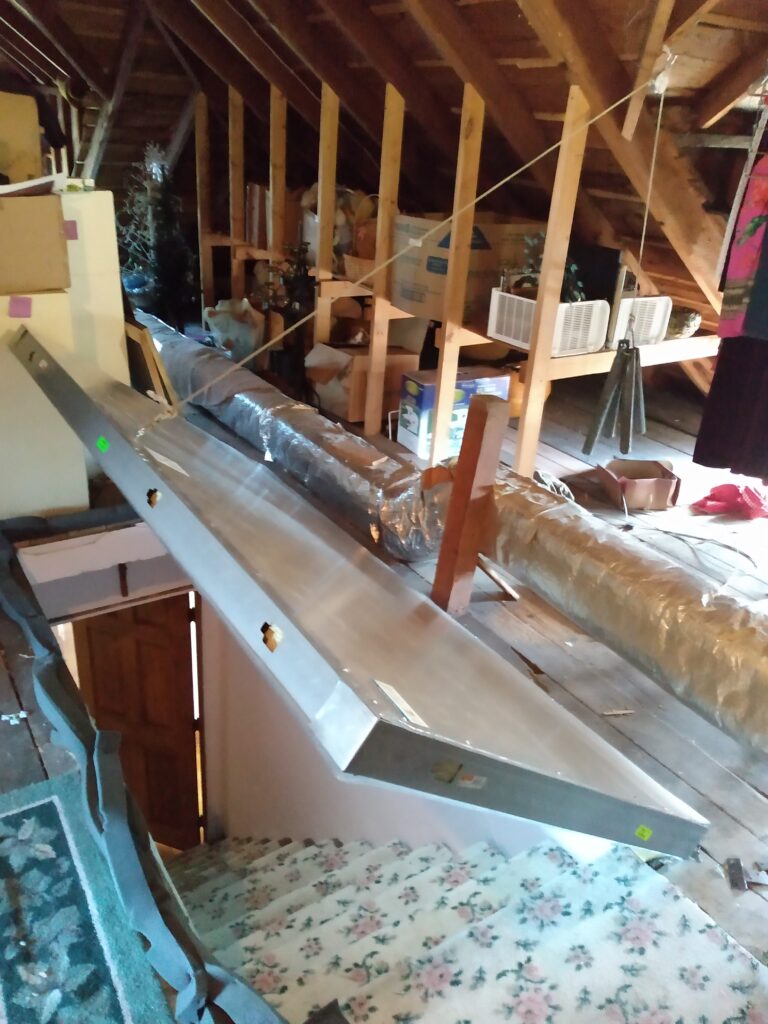 A steel and plastic door is suspended above the attic stairs.